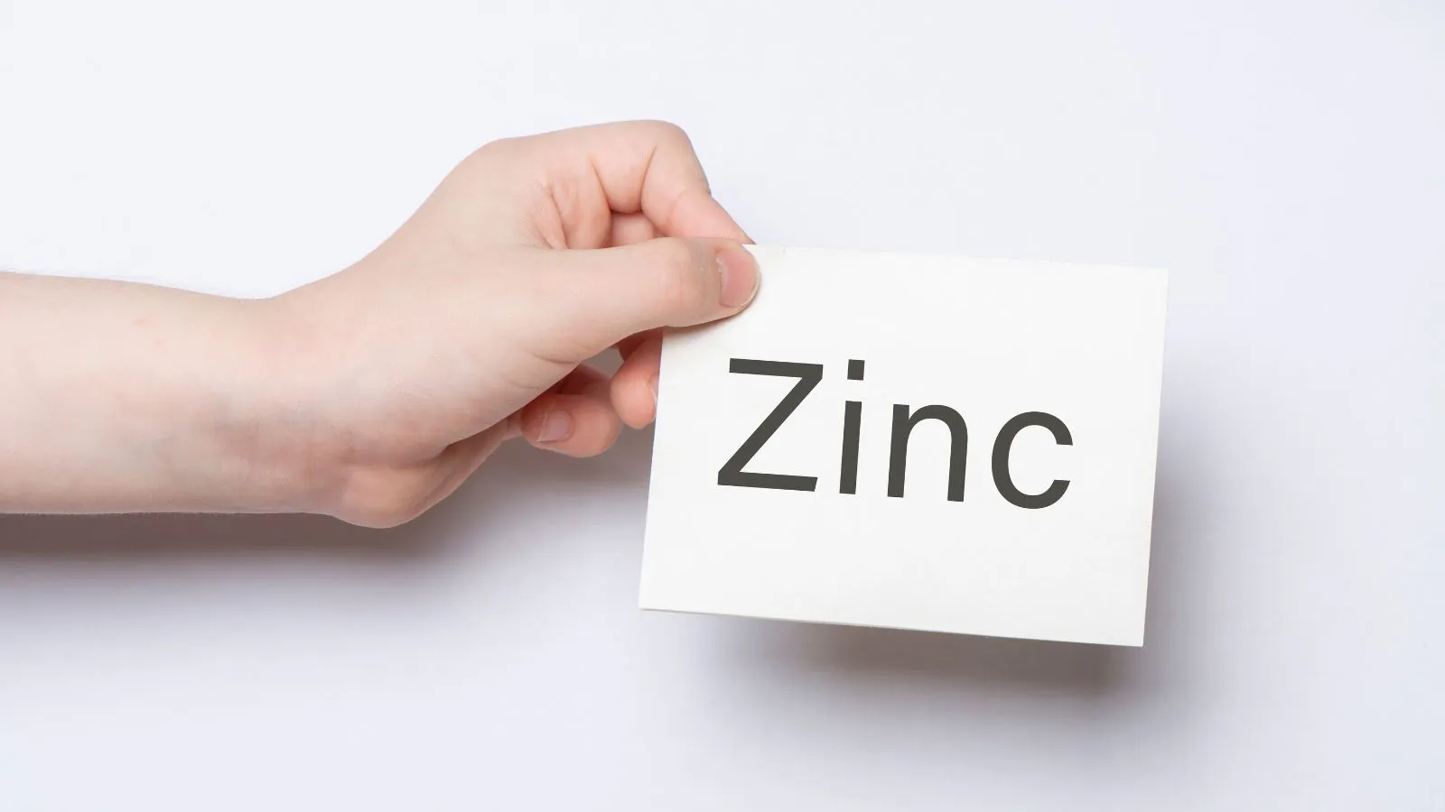 يد تحمل بطاقة بيضاء مكتوب عليها كلمة Zinc للدلالة على فوائد الزنك